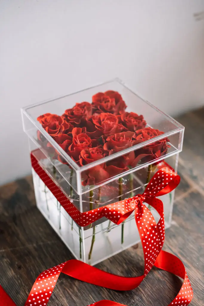 flower box filled with red roses with a red polka dotted bow on it standing on the rustic wooden table with grey wall on the background Limet akryl boks